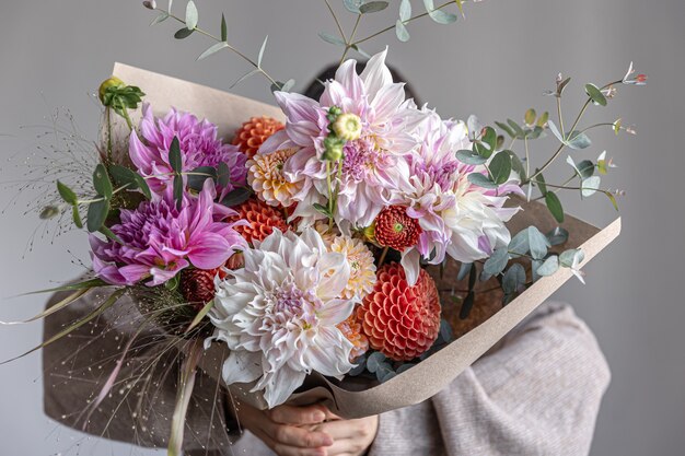 Une femme tient dans ses mains un grand bouquet de fête avec des chrysanthèmes et d'autres fleurs, en gros plan.