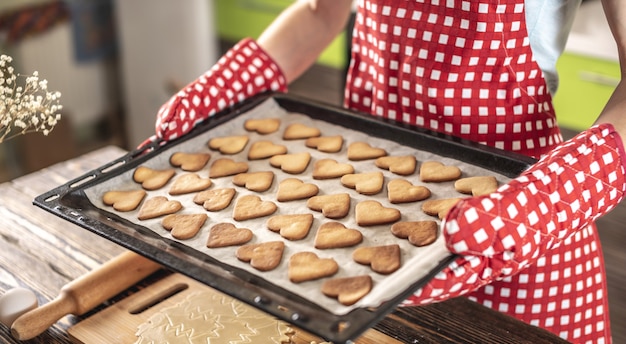 Femme tient dans ses mains une plaque à pâtisserie avec de délicieux biscuits faits maison en forme de coeur