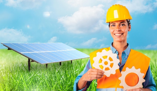 Une femme tient deux engrenages contre devant un panneau solaire