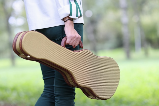 Une femme tient un étui pour violon et guitare et marche à travers les musiciens de rue du parc et la solitude