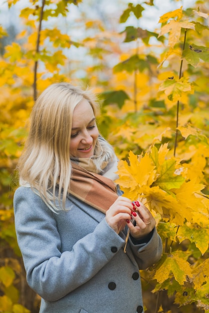 Une femme tient des feuilles jaunes d'érable dans ses mains dans un parc sur fond d'arbres