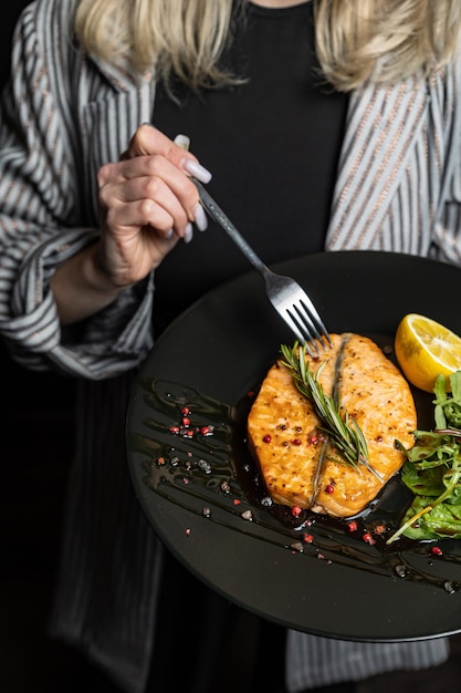 Une femme tient une fourchette et mange un repas de saumon.