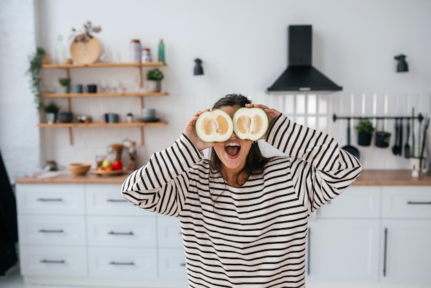 Une femme tient des fruits coupés au niveau des yeux au lieu de lunettes