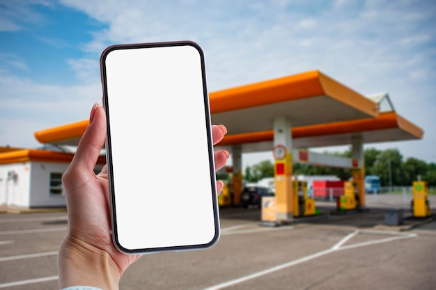 Une femme tient un gros plan d'un smartphone avec un écran blanc dans ses mains en toile de fond sur une station-service Maquette technologique pour les applications et les sites Web