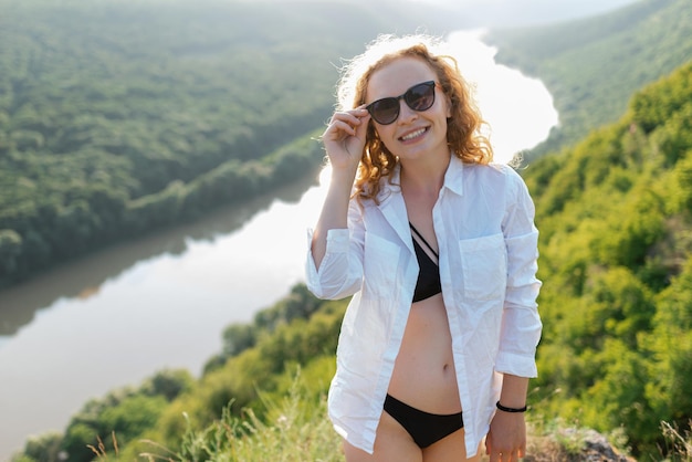 Une femme tient des lunettes de soleil en souriant et en regardant la caméra