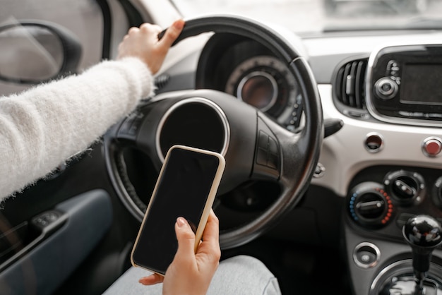 Une femme tient la main et utilise un téléphone portable dans une voiture personnelle sur le siège du conducteur. Vue rapprochée. Automobile de luxe moderne. Concept de conduite automobile.