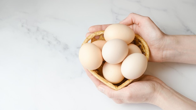 Une femme tient un panier de paille dans ses paumes avec de gros œufs de poule dans ses paumes Oeufs de poule de ferme