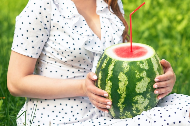 Femme tient la pastèque avec de la paille cocktail sur fond de sa robe blanche