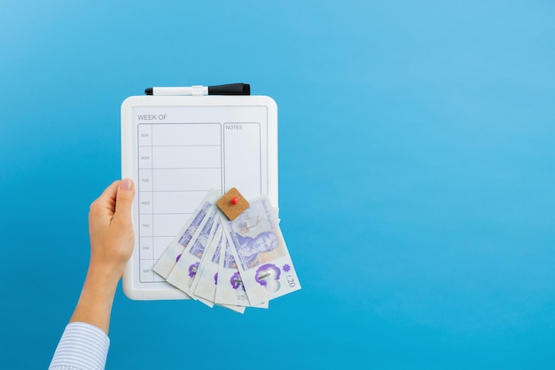 Une femme tient un planificateur hebdomadaire pour la semaine et des livres sterling dans ses mains dans un studio sur fond bleu Le concept de planification des dépenses pour la semaine