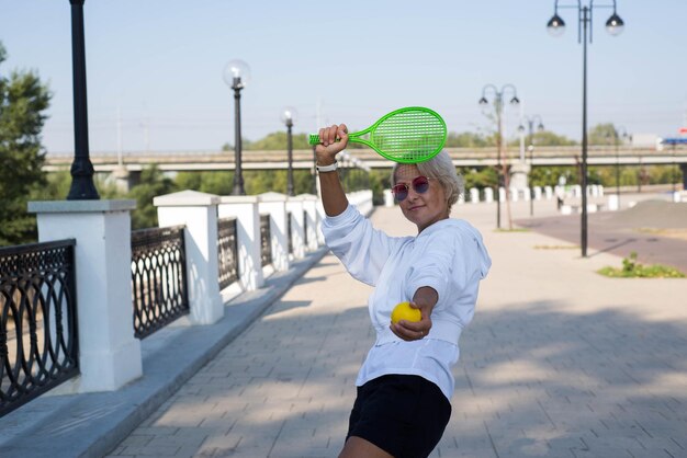 La femme tient une raquette et une balle en plein air.