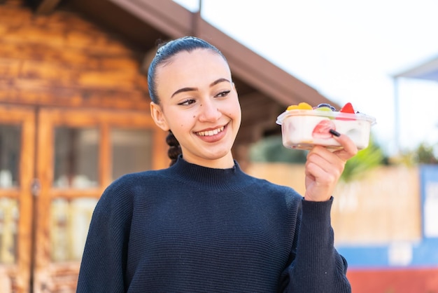 Une femme tient un récipient de fruits et sourit.