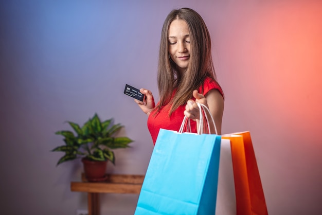 Femme tient des sacs multicolores avec des achats et une carte de crédit