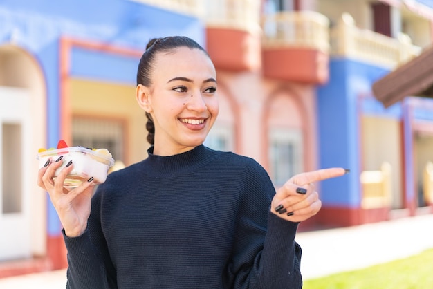 Une femme tient un sandwich et pointe vers la caméra.