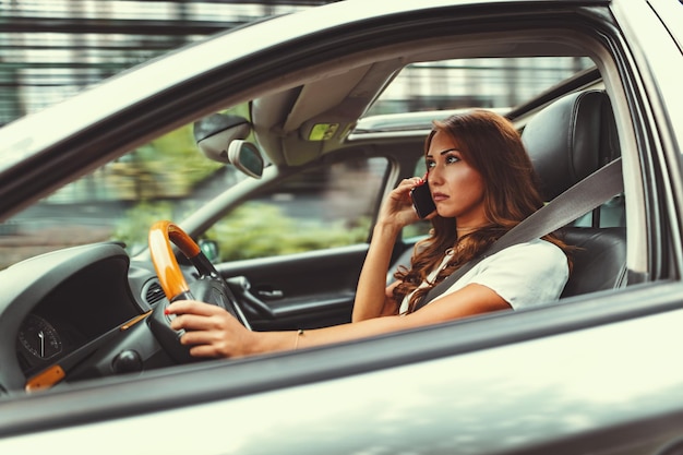 Une femme tient un smartphone dans sa main et parle pendant qu'elle conduit une voiture et se met en danger.