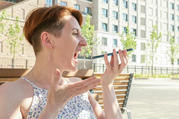 Une femme tient un smartphone près de sa bouche et crie furieusement dans le microphone