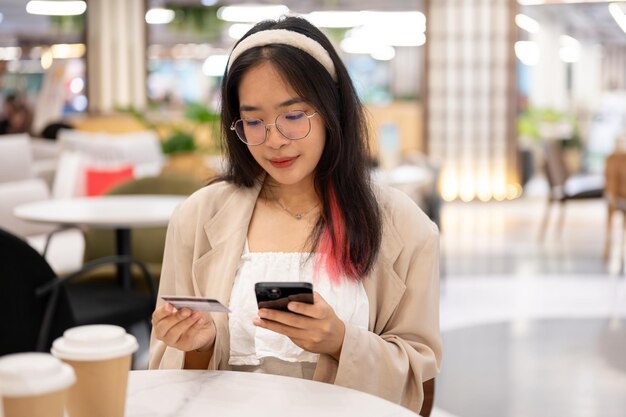 Une femme tient son smartphone et une carte de crédit alors qu'elle est assise dans un café du centre commercial