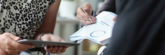 Femme tient la tablette dans les mains à côté des hommes avec un stylo à bille et des documents en mains en gros plan de bureau. Concept de signature de contrats commerciaux.