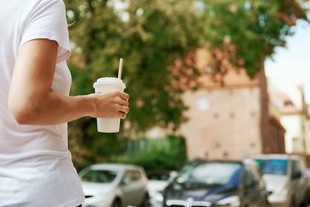 La femme tient la tasse de café de papier à la rue de ville