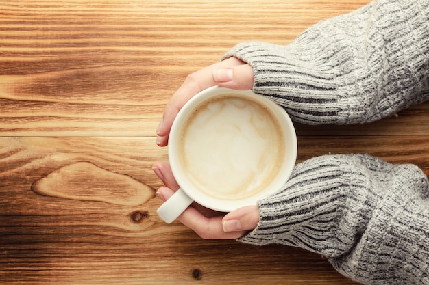 La femme tient une tasse de café sur une table en bois