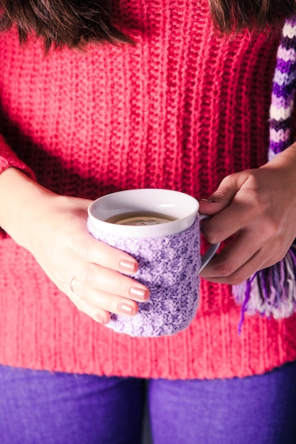 La femme tient une tasse de thé tricotée avec du citron