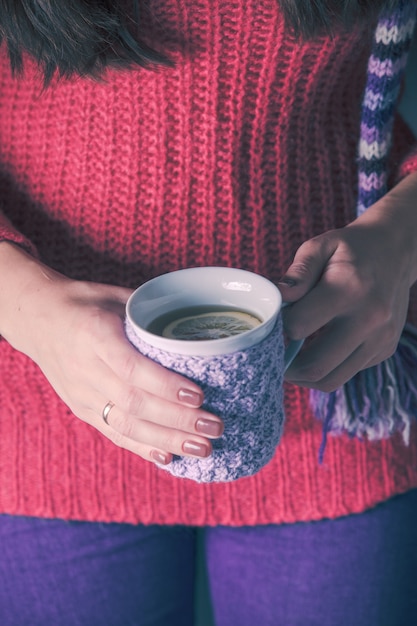 La femme tient une tasse de thé tricotée avec du citron