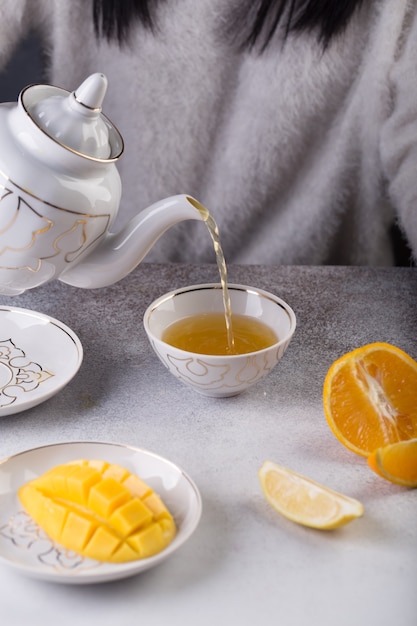 Femme tient une théière avec du thé dans sa main et le verse dans une tasse