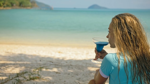 La femme tient un verre de cocktail de curaçao bleu sur la plage mer bleu azur d'une île tropicale Beau fond de bord de mer flou Célébrez le concept de vacances d'été de voyage d'agrément se détendre