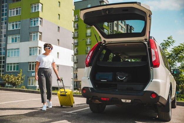 Femme tirez la valise sur roues pour voyager sur la route du coffre de la voiture