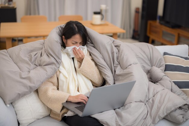 Une femme tombe malade et éternue en utilisant un ordinateur portable à la maison.