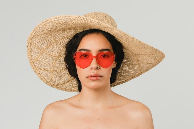 Femme torse nu portant un grand chapeau rond et des lunettes de soleil en forme de coeur vintage rouge