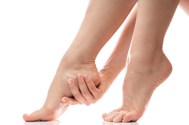 Femme touchant doucement la peau douce de son talon Pieds féminins sur fond blanc