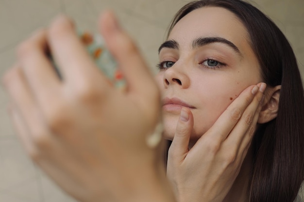 Photo femme touchant le visage et regardant dans le miroir tout en faisant des soins de la peau routine de beauté quotidienne