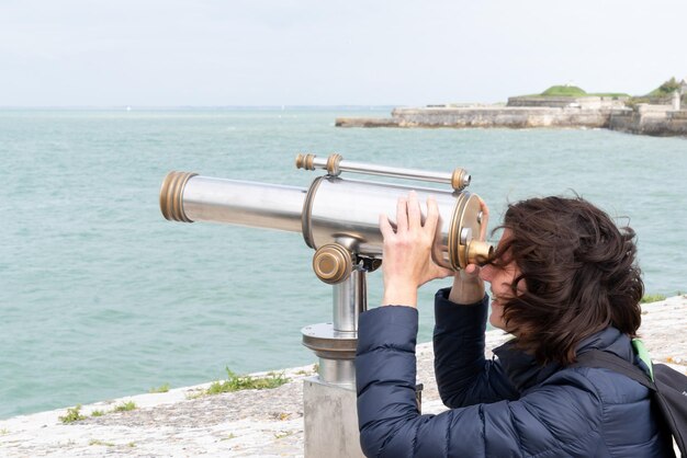 Femme de tourisme regardant à travers des jumelles à monnayeur pendant les vacances à la mer