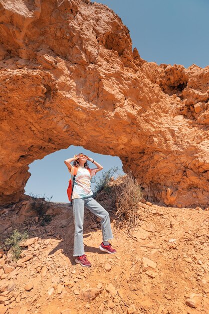 Photo femme de tourisme avec sac à dos se promène le long d'un sentier dans un canyon désert avec une arche majestueuse de roches rouges sentier de randonnée et les dangers du trekking en solo