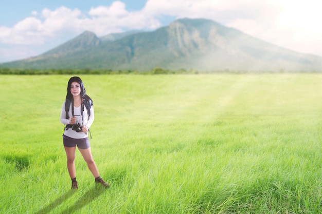 Une femme touriste asiatique marche sur un sentier de colline verdoyant avec un sac à dos et un appareil photo