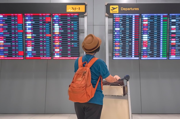 Femme touriste avec chariot à bagages regardant le panneau d'information de vol à l'aéroport international