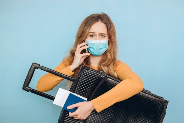 femme touriste dans un masque médical est assis avec des bagages dans ses mains. Éclosion de coronavirus COVID-19. Concept de voyage et de couronne. Un touriste ne peut pas partir en raison d'une pandémie.