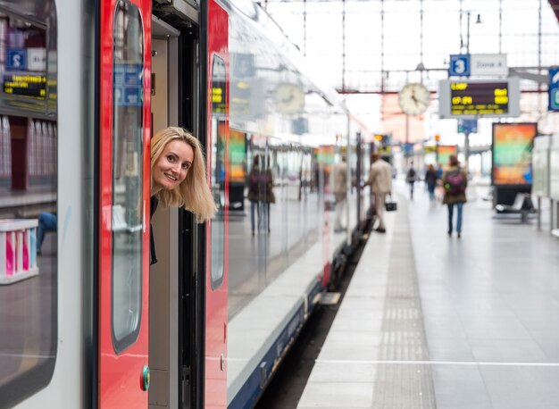 Femme touriste regarde hors du train sur la plate-forme de la gare, voyage en Europe. Transport par les chemins de fer européens, tourisme confortable