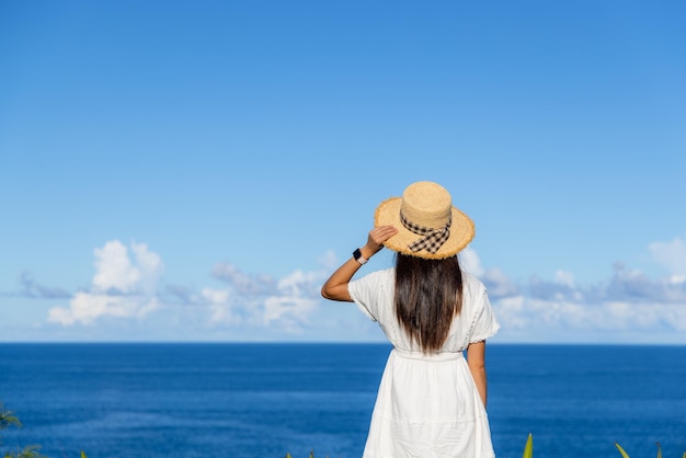 Femme touriste en robe blanche et regardant la mer en été