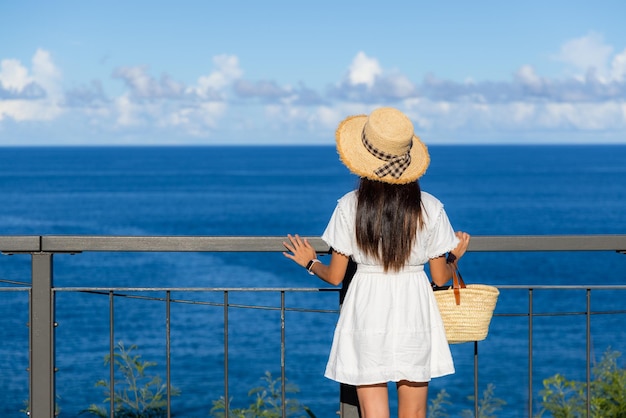 Femme touriste en robe blanche et regardant la mer en été