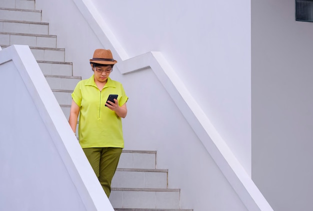 Femme touriste vintage utilisant un smartphone en descendant les escaliers à l'extérieur du bâtiment blanc