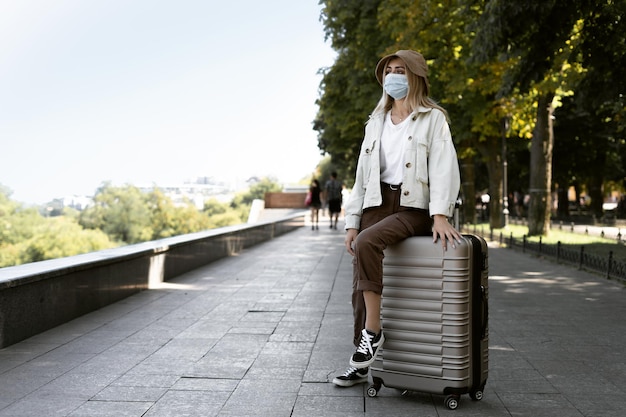 Femme touristique dans une ville européenne, tourisme en Europe. une jeune fille vêtue d'un masque de protection médicale est assise sur une grande valise.