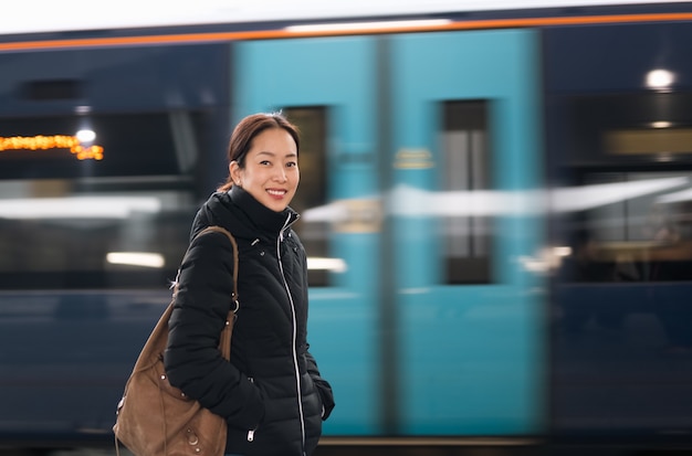 Femme touristique heureuse debout sur la plate-forme avec un train en mouvement flou sur fond