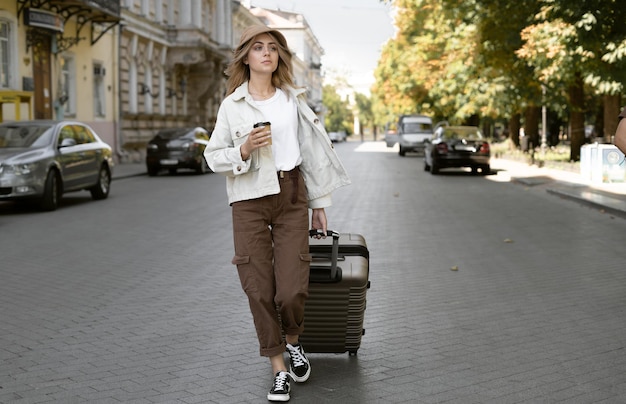 Femme touristique avec une valise dans la rue dans une ville européenne, tourisme en Europe. marche dans la rue en tirant des bagages avec lui. café dans un gobelet en papier jetable.