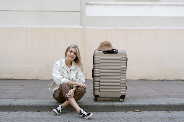 Femme touristique avec une valise dans une ville européenne, tourisme en Europe. Assis sur le trottoir à côté d'une grosse valise en regardant le photographe.