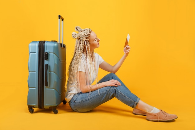 Femme touristique en vêtements décontractés d'été avec passeport assis près de grande valise isolée
