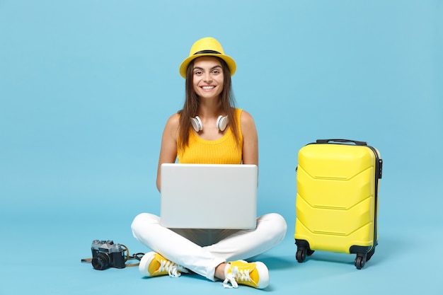 Femme touristique voyageur en vêtements décontractés jaunes, chapeau avec appareil photo pour ordinateur portable valise ordinateur portable sur bleu