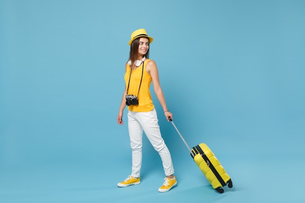 Femme touristique voyageur en vêtements décontractés jaunes, chapeau avec appareil photo valise sur bleu