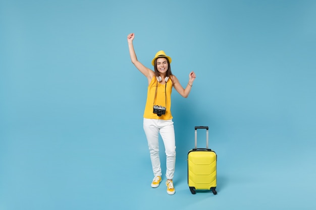 Femme touristique voyageur en vêtements décontractés jaunes, chapeau avec appareil photo valise sur bleu