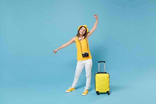 Femme touristique voyageur en vêtements décontractés jaunes, chapeau avec appareil photo valise sur bleu